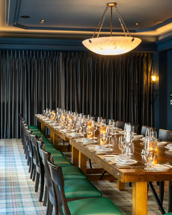 Een lange gedekte tafel met kaarslicht in een zaal met donkere gordijnen